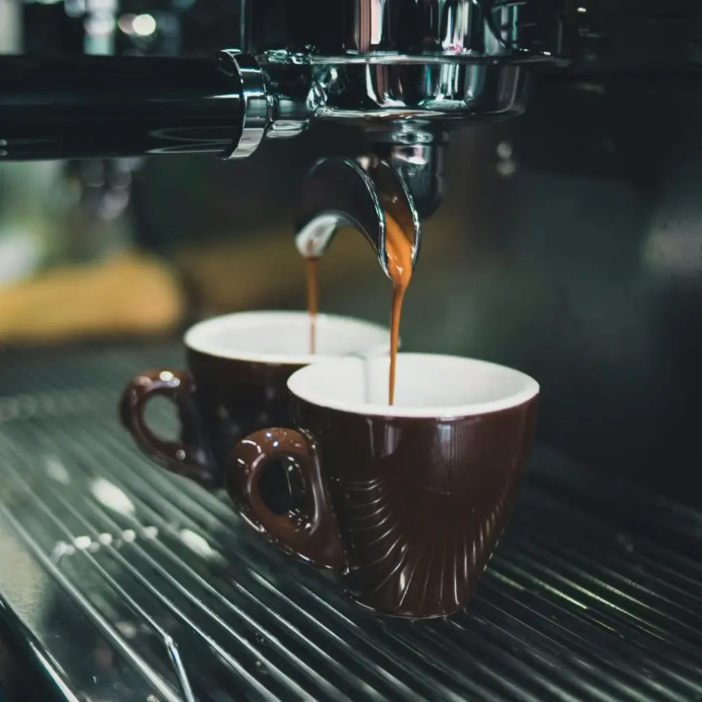 A close-up of two espresso cups placed under a coffee machine, with dark coffee pouring into them.