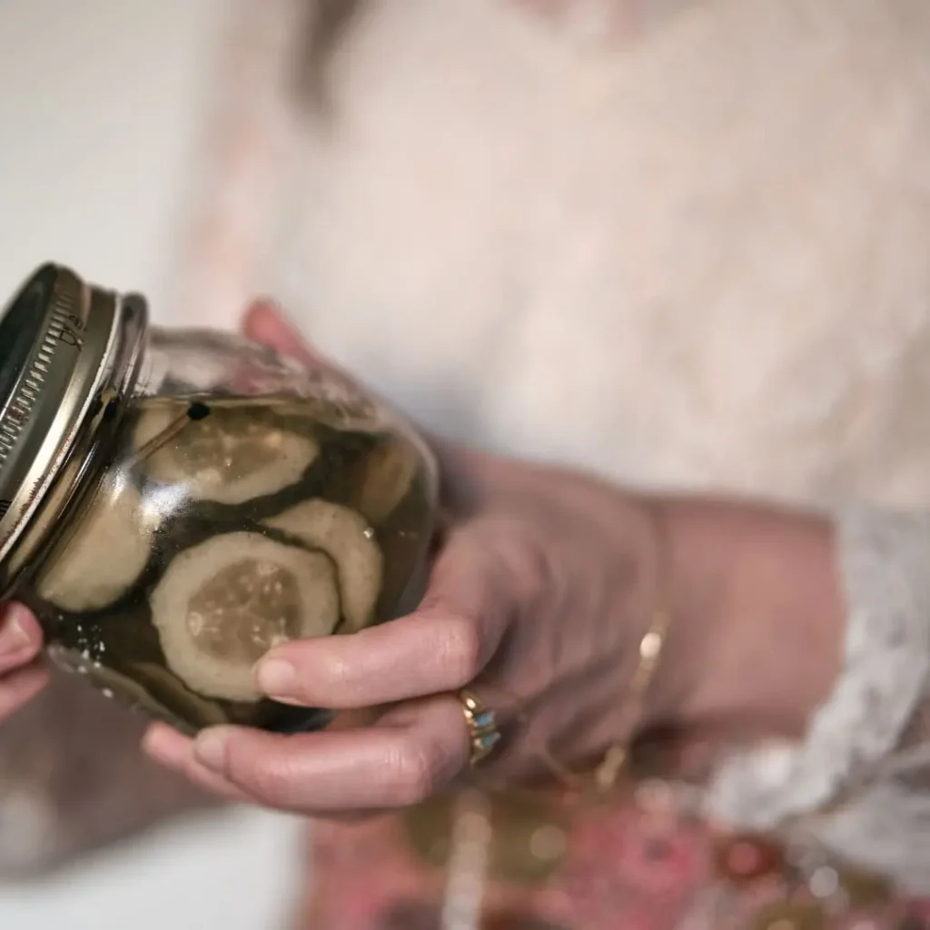 A close-up of a person holding a jar of pickles, showcasing the contents through the clear glass jar. The pickles are thinly sliced, arranged neatly, and submerged in brine.