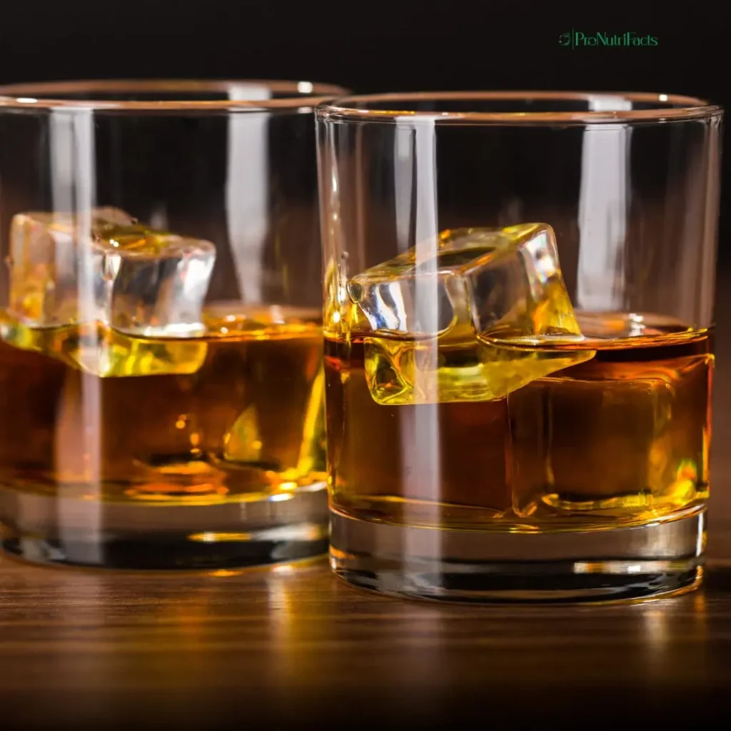 A close-up of two glasses filled with whiskey and ice cubes on a wooden surface, with warm lighting reflecting off the glass. The image conveys the concept of alcohol consumption.