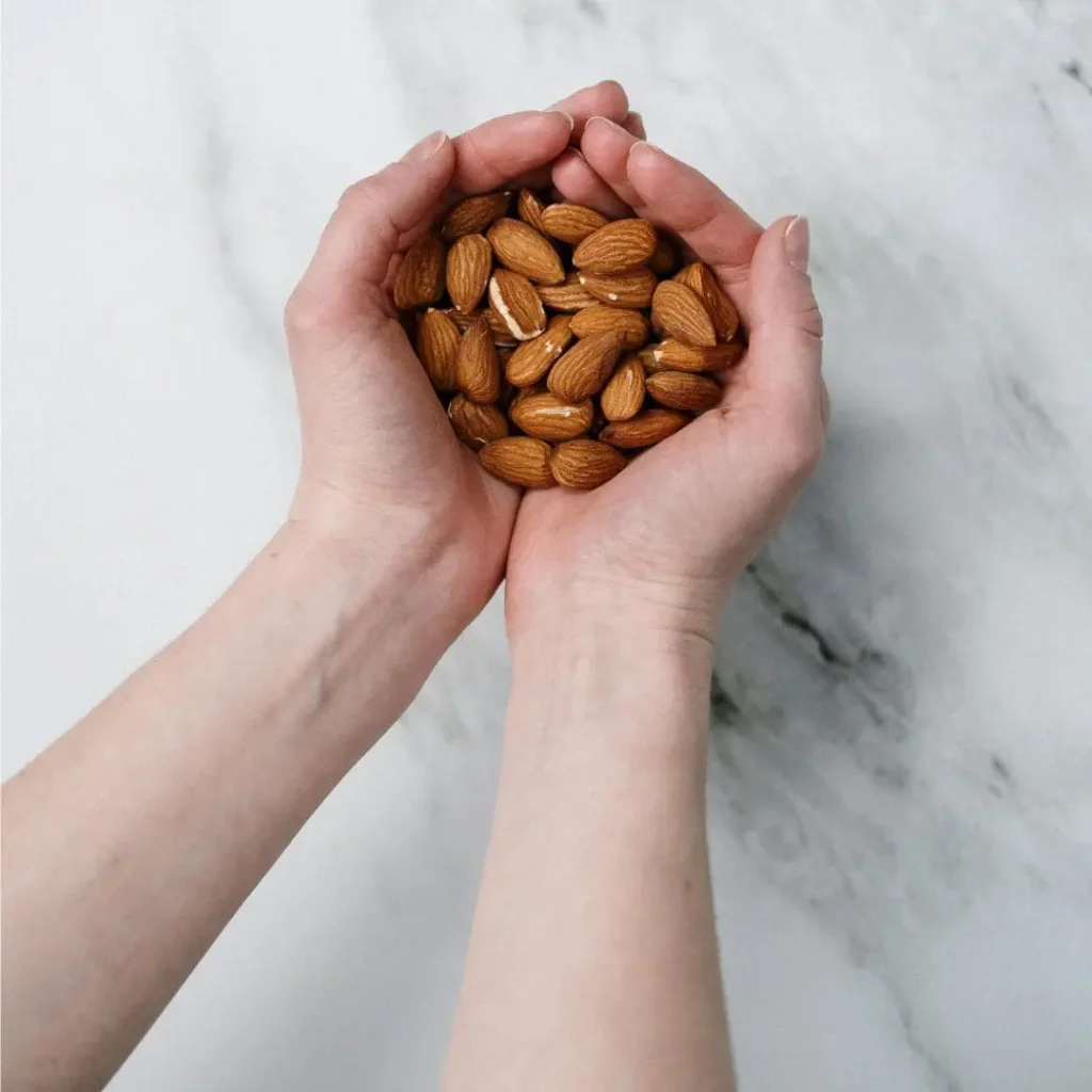 Two hands gently cupping a handful of raw almonds against a marble surface. Text overlay reads: 'Are Almonds Good for Weight Loss? How Many to Eat.