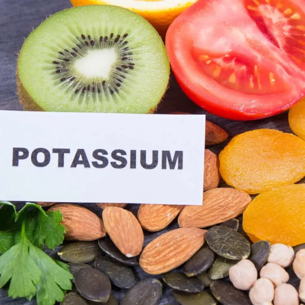 A variety of potassium-rich foods, including kiwi, tomato, dried apricots, almonds, and seeds, arranged around a label that reads " Potassium Supplements " This image emphasizes natural sources of potassium essential for a healthy diet.