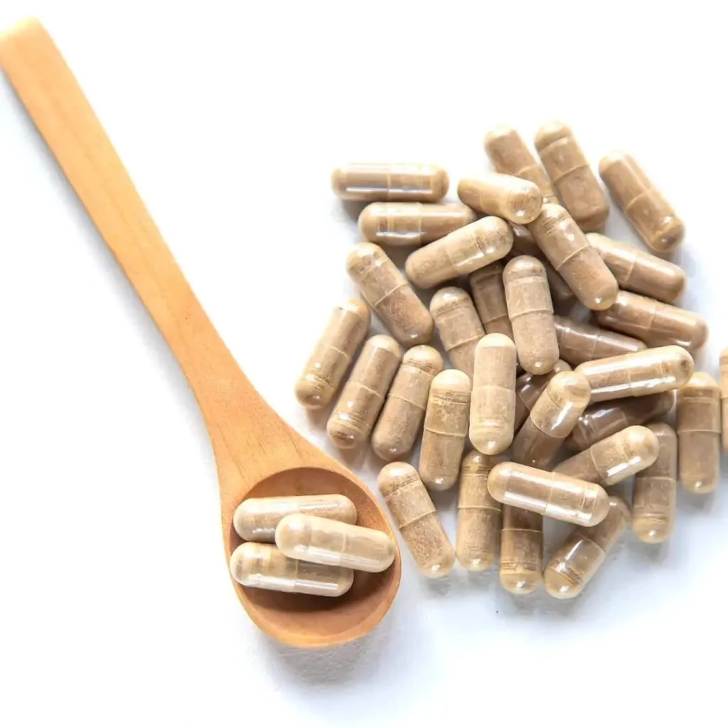 A wooden spoon filled with natural supplement capsules, surrounded by more capsules on a white background, representing dietary supplements that support overall wellness.